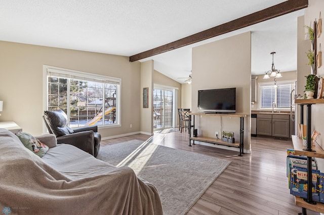 living area with a ceiling fan, vaulted ceiling with beams, wood finished floors, a textured ceiling, and baseboards