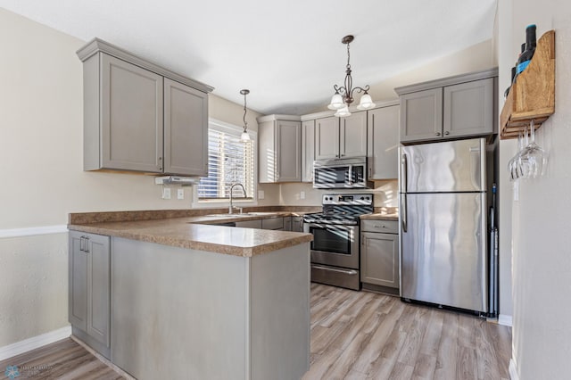 kitchen featuring decorative light fixtures, stainless steel appliances, gray cabinetry, light wood-style floors, and a peninsula