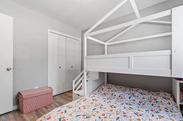 bedroom with a closet, a textured ceiling, wood finished floors, and vaulted ceiling