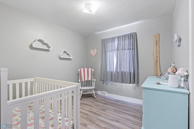 bedroom featuring baseboards, a nursery area, a textured ceiling, visible vents, and wood finished floors