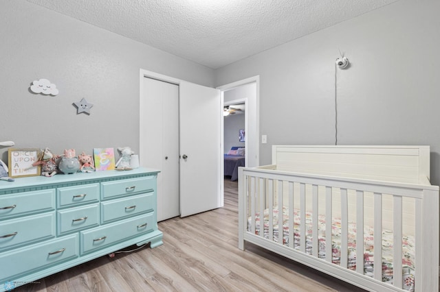 bedroom featuring light wood finished floors, a nursery area, a closet, and a textured ceiling