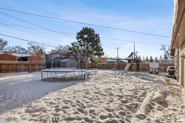 snowy yard with a fenced backyard, a playground, an outbuilding, and a trampoline