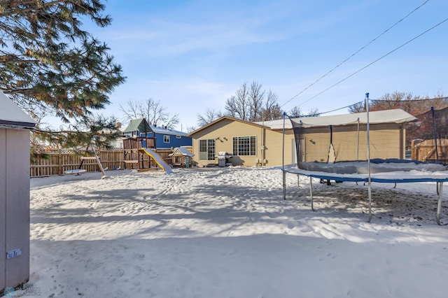 snow covered property with a trampoline, a playground, and fence