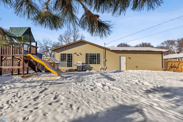 snow covered back of property featuring fence and a playground