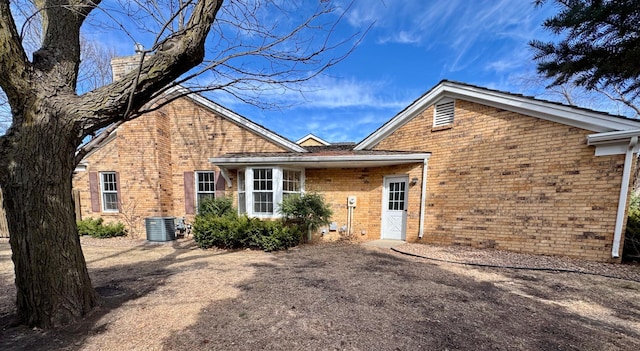 back of house with brick siding, central AC unit, and a chimney