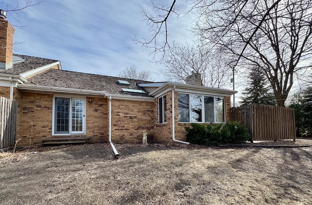 view of side of home with a chimney, fence, and brick siding