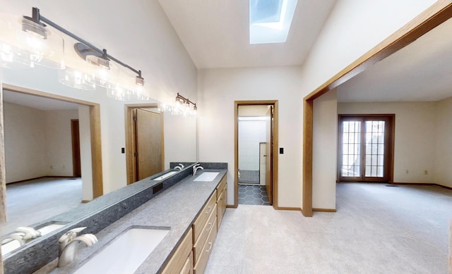 bathroom with baseboards, double vanity, a sink, and a skylight