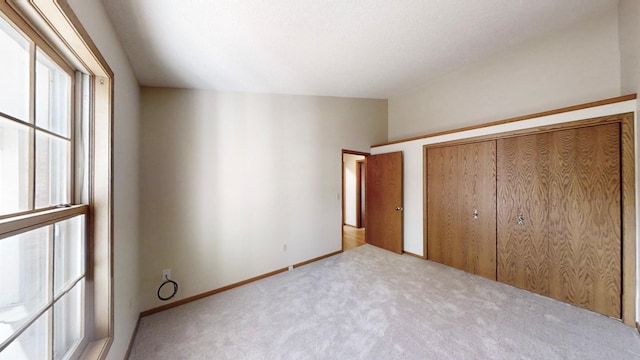 unfurnished bedroom featuring a closet, lofted ceiling, carpet flooring, and baseboards