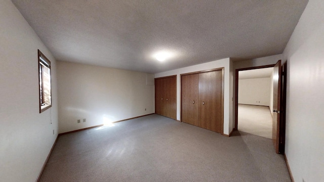 unfurnished bedroom featuring light colored carpet, multiple closets, and a textured ceiling
