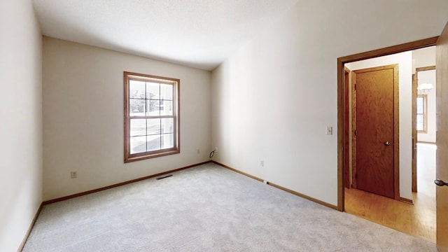 empty room with light colored carpet, visible vents, and baseboards