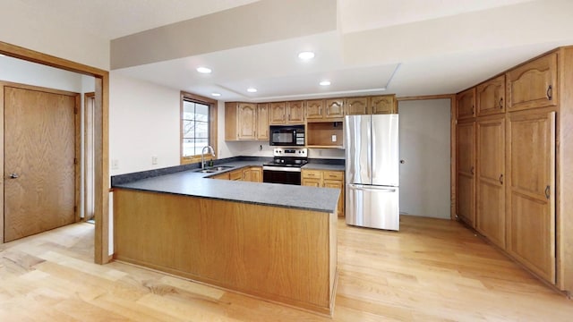 kitchen with a peninsula, dark countertops, appliances with stainless steel finishes, a sink, and light wood-style floors