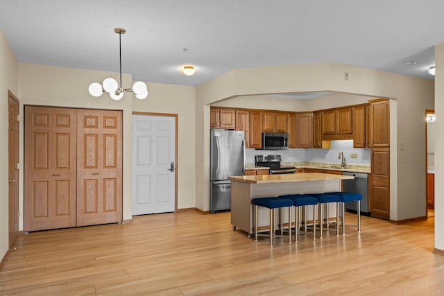 kitchen featuring light countertops, light wood-type flooring, decorative backsplash, a kitchen island, and appliances with stainless steel finishes