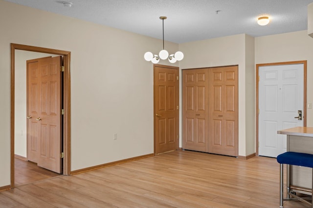 foyer entrance with baseboards, light wood-style floors, a chandelier, and a textured ceiling