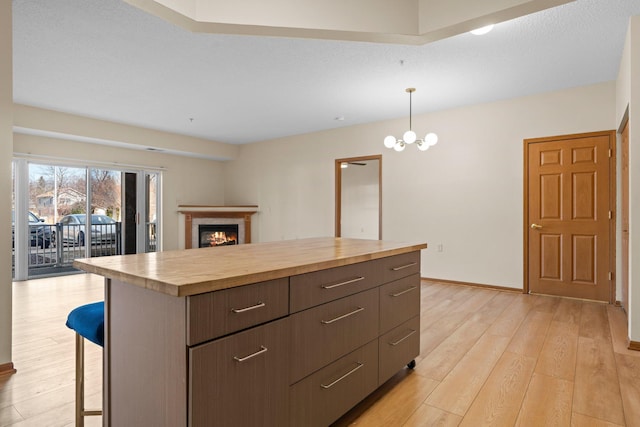 kitchen featuring open floor plan, hanging light fixtures, wood counters, light wood finished floors, and a warm lit fireplace