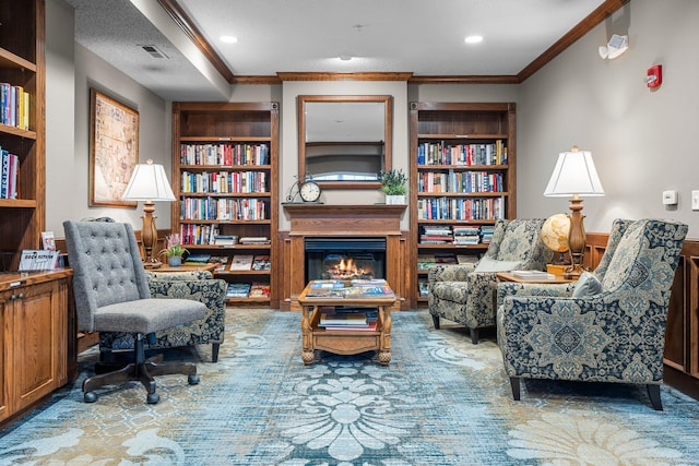 sitting room featuring crown molding, built in shelves, visible vents, a glass covered fireplace, and wainscoting