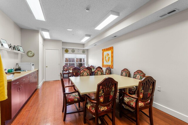 dining area with baseboards, visible vents, light wood-style flooring, and a textured ceiling