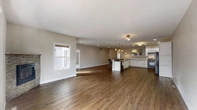 unfurnished living room featuring dark wood-type flooring, a fireplace, baseboards, and recessed lighting