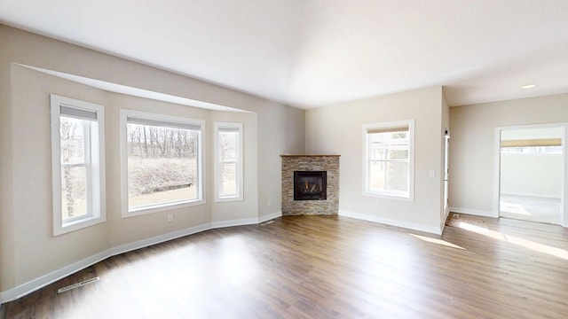 unfurnished living room with a stone fireplace, baseboards, and wood finished floors