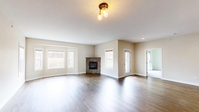 unfurnished living room featuring a stone fireplace, baseboards, and dark wood finished floors
