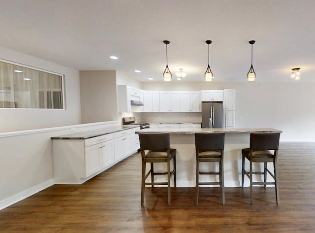 kitchen featuring white cabinets, a kitchen bar, appliances with stainless steel finishes, under cabinet range hood, and dark wood-style floors