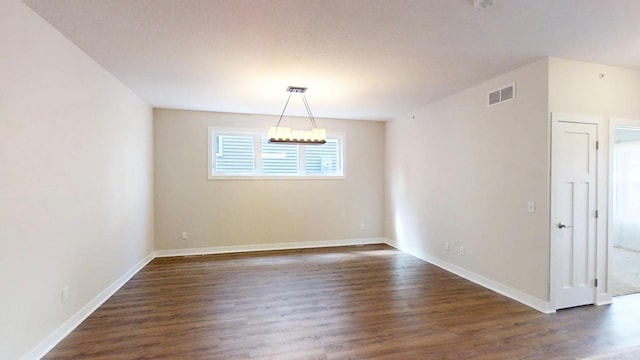 empty room featuring dark wood-style flooring, a notable chandelier, baseboards, and visible vents