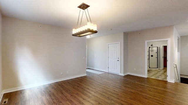empty room featuring a notable chandelier, baseboards, and wood finished floors
