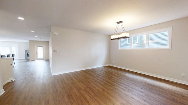 spare room with baseboards, dark wood-style floors, recessed lighting, and a notable chandelier