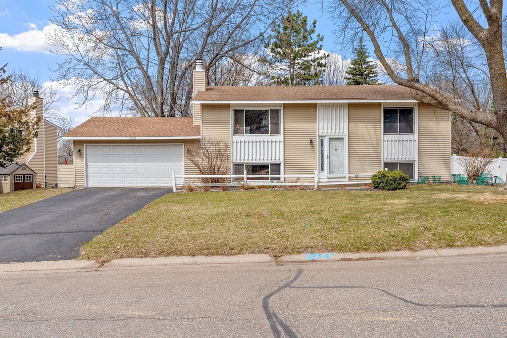 view of front of home with a chimney, aphalt driveway, a front yard, a garage, and fence