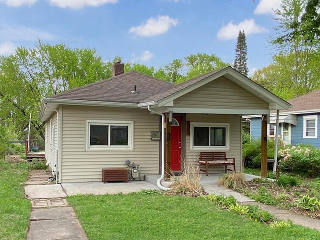 view of front facade with a chimney, a porch, a front yard, and a shingled roof