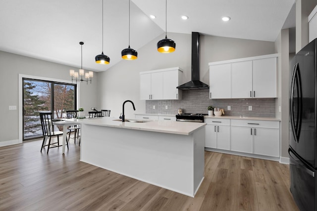 kitchen featuring wall chimney range hood, freestanding refrigerator, a sink, light countertops, and tasteful backsplash