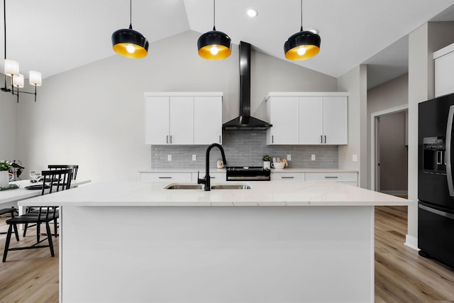 kitchen with wall chimney exhaust hood, black fridge with ice dispenser, a sink, stainless steel stove, and tasteful backsplash