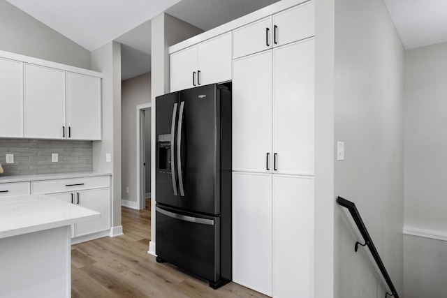 kitchen featuring black fridge with ice dispenser, backsplash, light stone counters, and white cabinetry