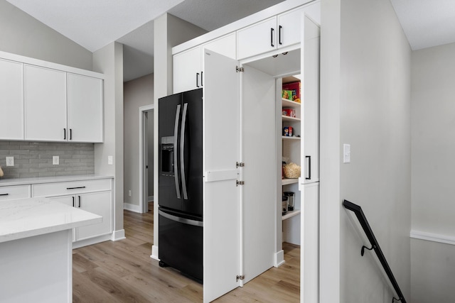 kitchen with black refrigerator with ice dispenser, tasteful backsplash, light wood finished floors, and white cabinetry