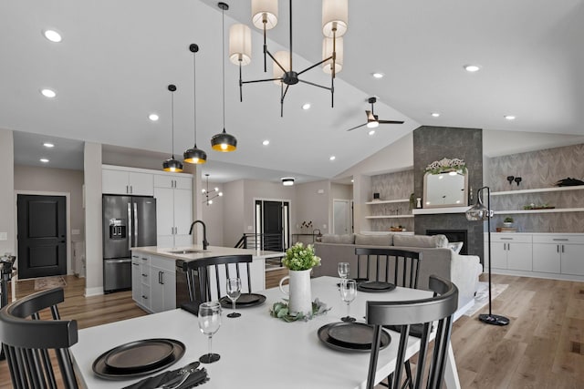 dining area featuring lofted ceiling, a tiled fireplace, light wood-type flooring, a ceiling fan, and recessed lighting