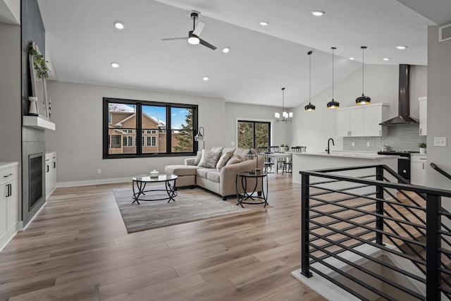 living room featuring vaulted ceiling, a ceiling fan, light wood-style flooring, a glass covered fireplace, and recessed lighting