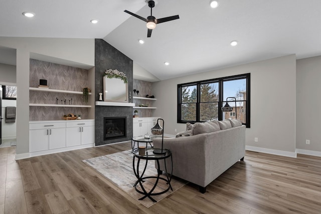 living area featuring built in features, a tile fireplace, baseboards, a ceiling fan, and light wood-type flooring