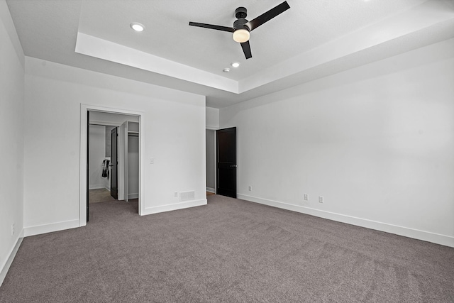 unfurnished bedroom with a tray ceiling, dark carpet, baseboards, recessed lighting, and a walk in closet