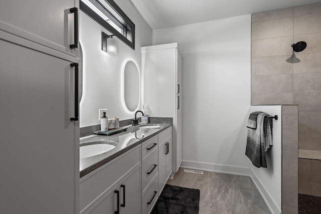 bathroom featuring walk in shower, double vanity, wood finished floors, and baseboards