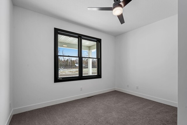 empty room with dark colored carpet, ceiling fan, and baseboards