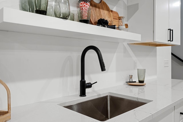 kitchen view of a sink, white cabinets, and light stone countertops