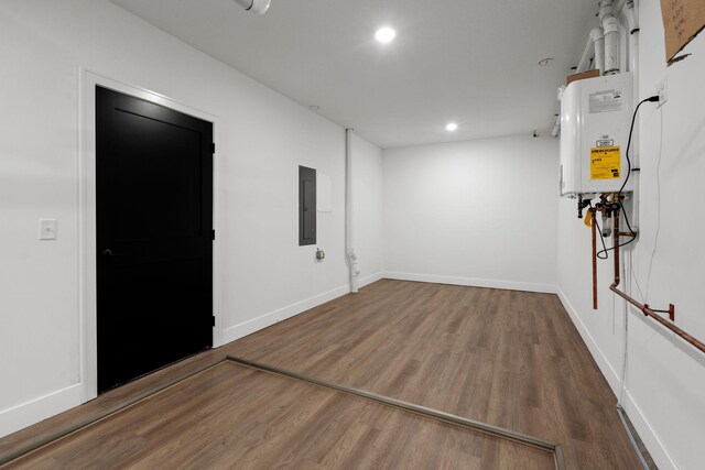 empty room with electric panel, tankless water heater, wood finished floors, recessed lighting, and baseboards