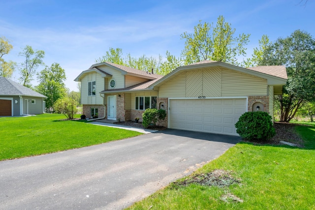 split level home featuring brick siding, asphalt driveway, a garage, a front yard, and a shingled roof