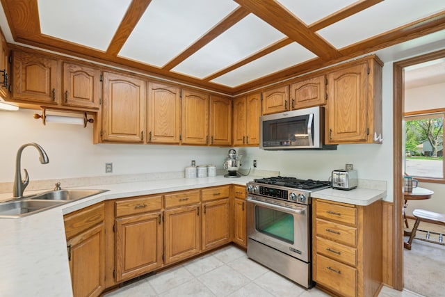 kitchen with appliances with stainless steel finishes, a sink, light countertops, and brown cabinetry