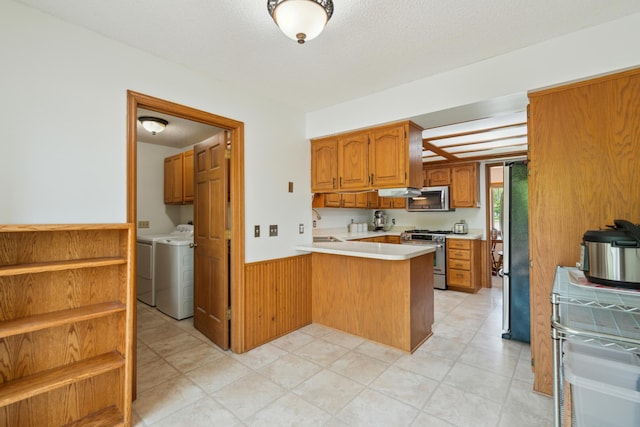 kitchen featuring appliances with stainless steel finishes, a peninsula, light countertops, independent washer and dryer, and wainscoting