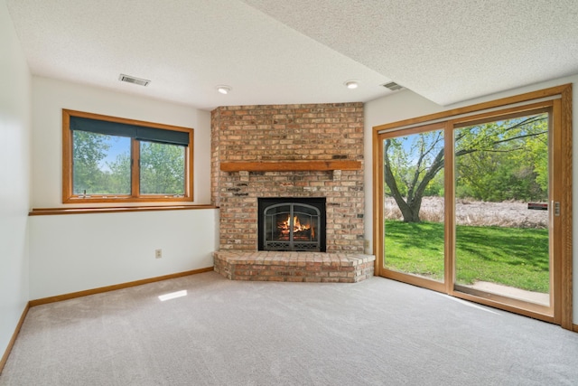 unfurnished living room with plenty of natural light, carpet, a brick fireplace, a textured ceiling, and baseboards