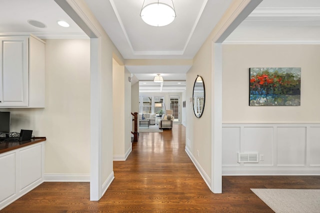 hallway featuring dark wood-type flooring, a decorative wall, visible vents, and wainscoting