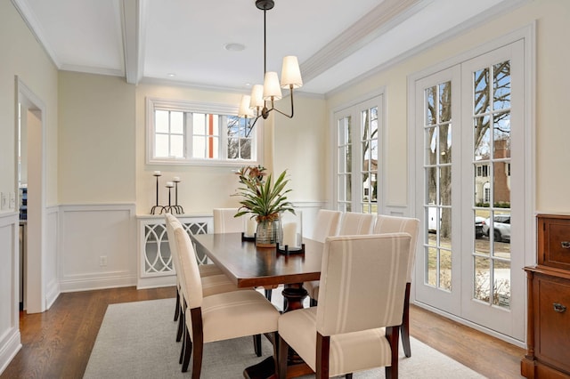 dining room featuring crown molding, an inviting chandelier, dark wood-style flooring, a decorative wall, and wainscoting