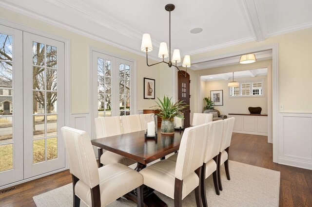 dining space with a wainscoted wall, crown molding, beam ceiling, dark wood-style floors, and a decorative wall