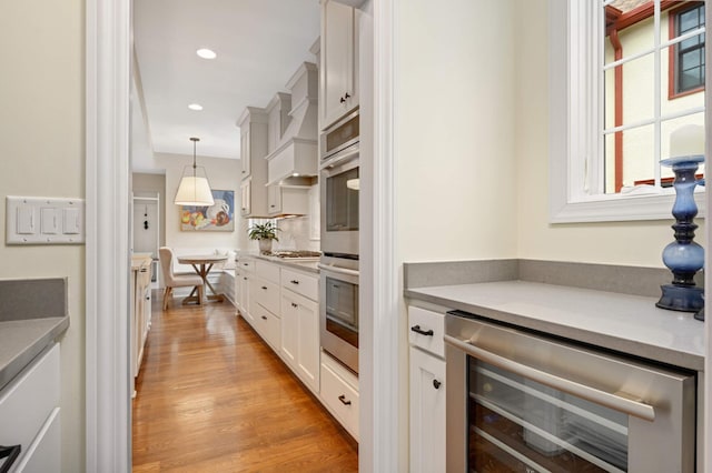 kitchen featuring white cabinetry, beverage cooler, decorative light fixtures, light wood-style floors, and recessed lighting