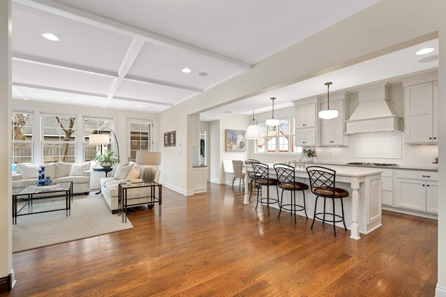 kitchen featuring coffered ceiling, a breakfast bar, custom exhaust hood, and dark wood-style flooring